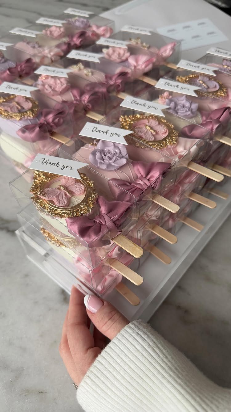 Pink and purple cake pops with thank you tags in a clear box.