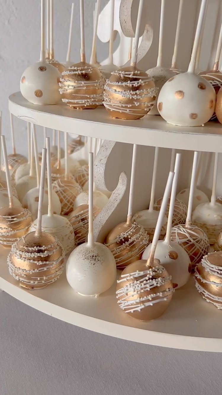 Gold and white cake pops arranged on a tiered white dessert stand.