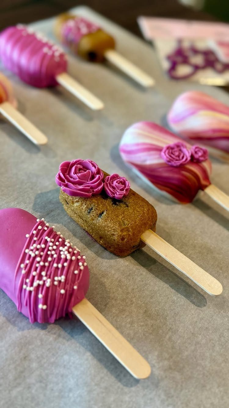 Assorted pink and brown cake pops with frosting roses on parchment paper.