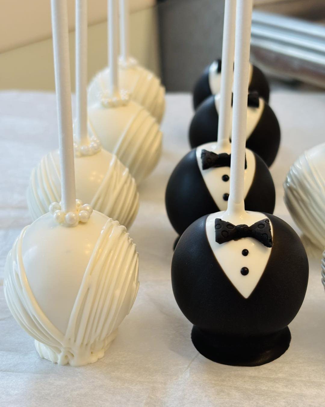 Cake pops decorated as white wedding dresses and black tuxedos with bow ties.