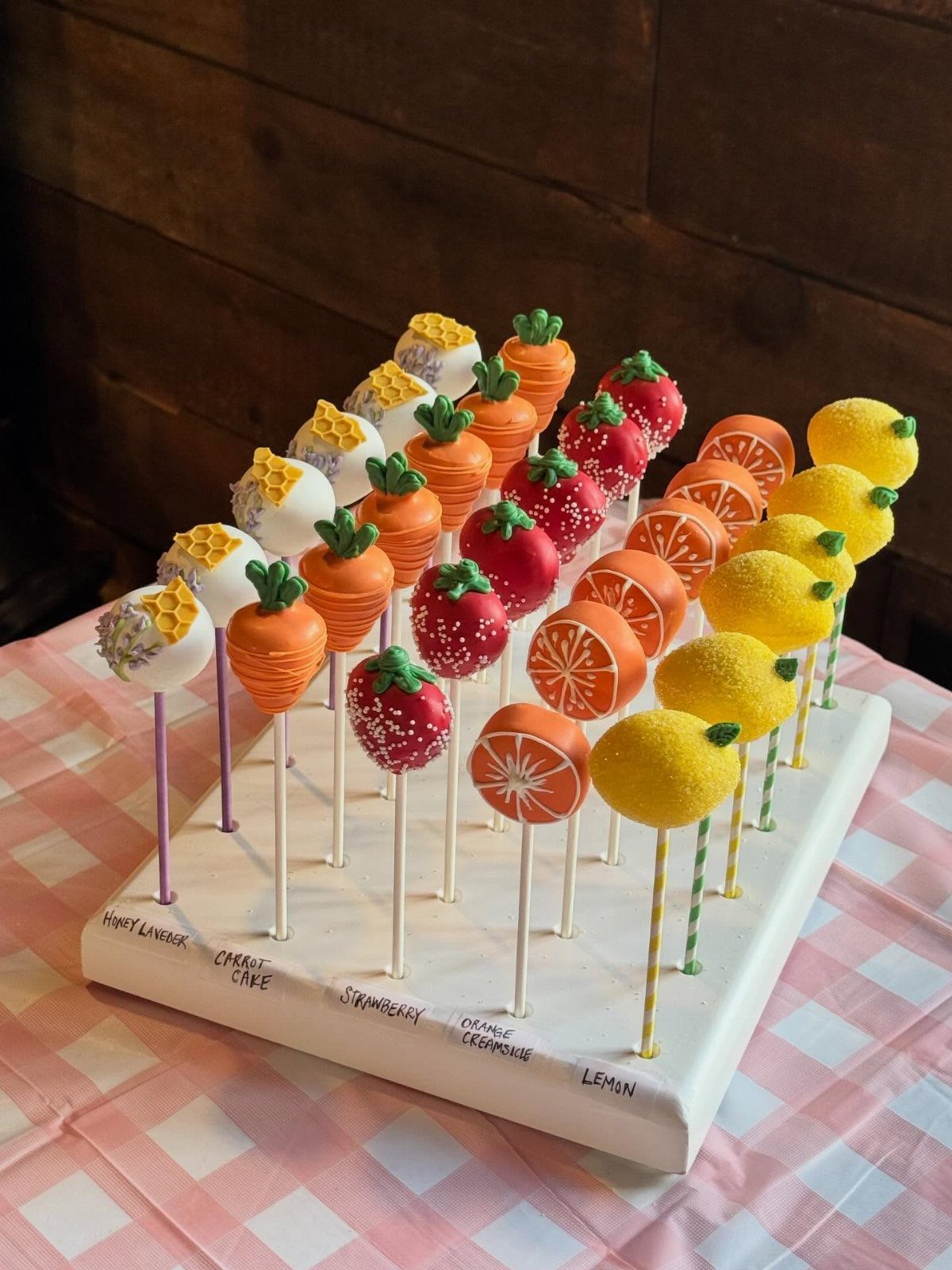 Fruit-shaped cake pops in various colors arranged on a white display stand.