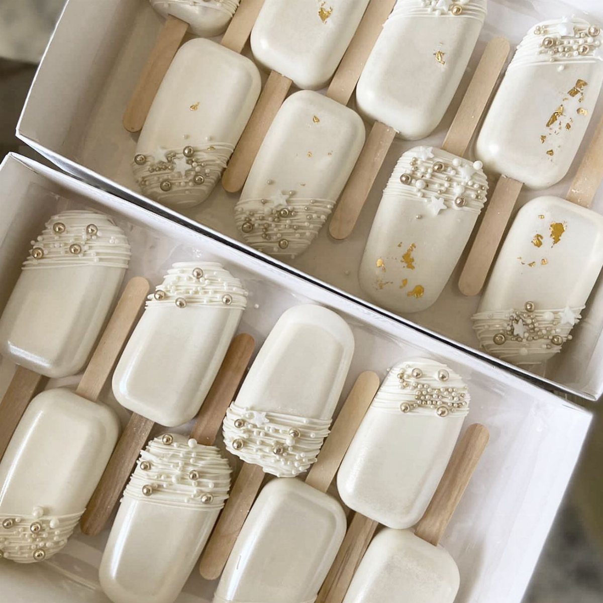 White chocolate cake pops with gold sprinkles and leaf in white boxes