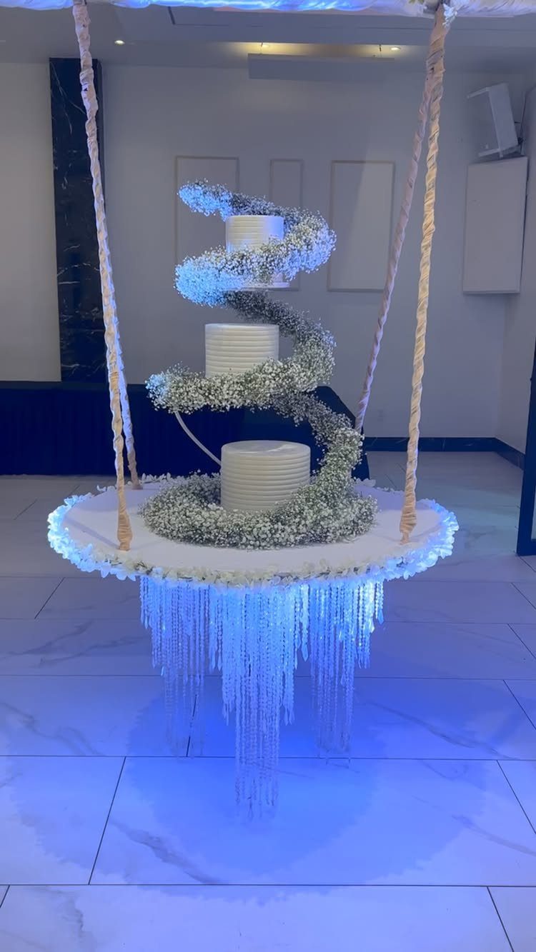 Three-tier white wedding cake on a suspended swing platform with spiral baby's breath flowers.