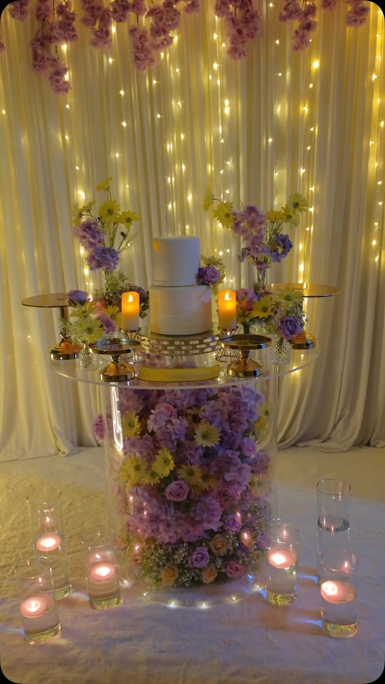 White wedding cake on a clear flower-filled table with fairy light backdrop