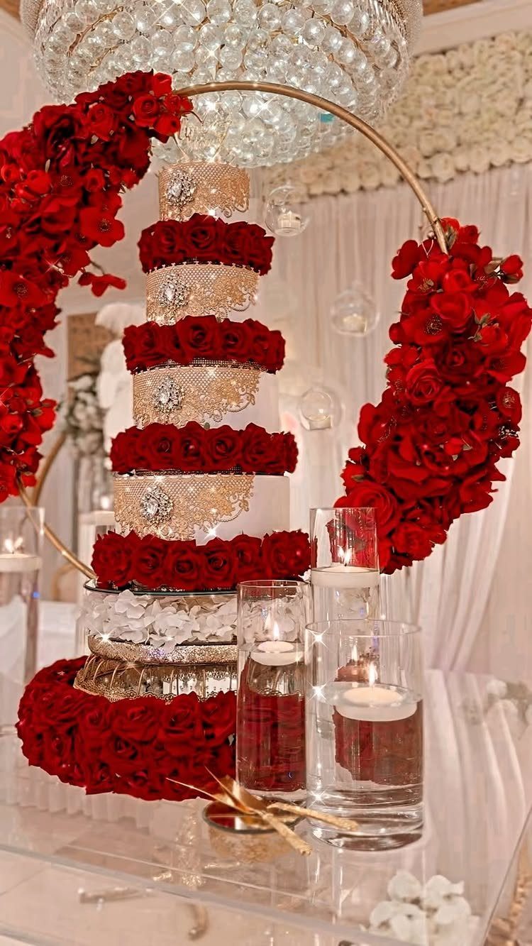 Tiered wedding cake with red roses on a clear table with floating candles.