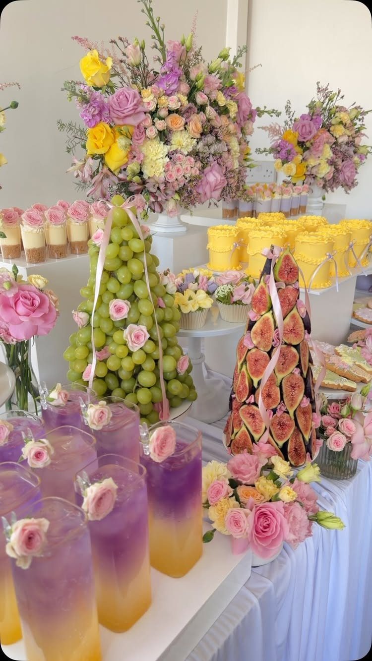 Dessert table with grape and fig towers, colorful drinks, and floral arrangements.