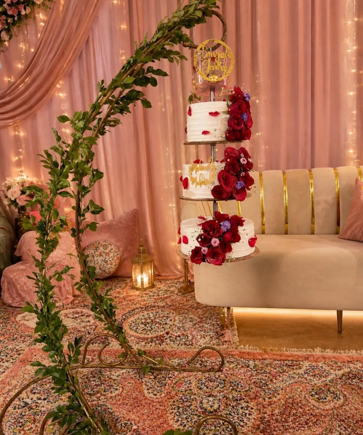 Three-tiered white wedding cake with red flowers on a gold stand in a lounge