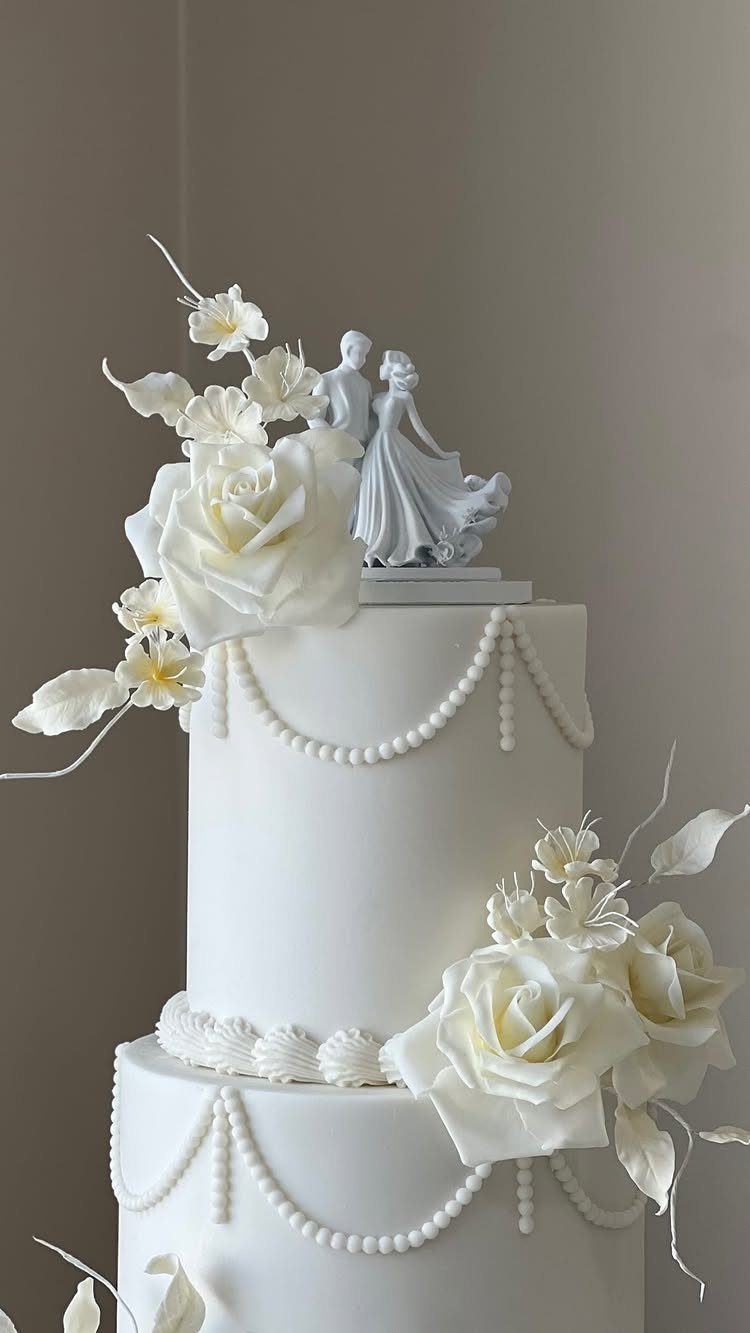 White tiered wedding cake with sugar roses, pearl icing details, and a couple topper.