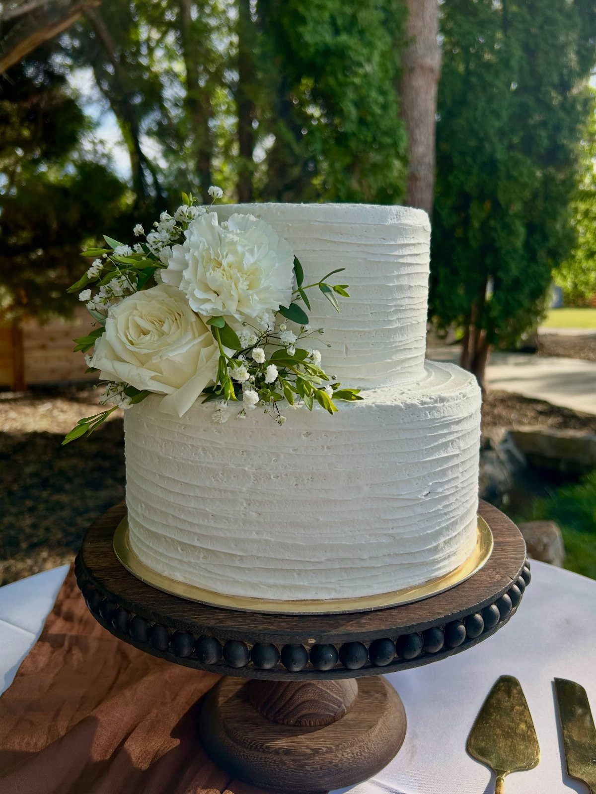 Two-tier white textured cake decorated with white roses on a wooden stand.