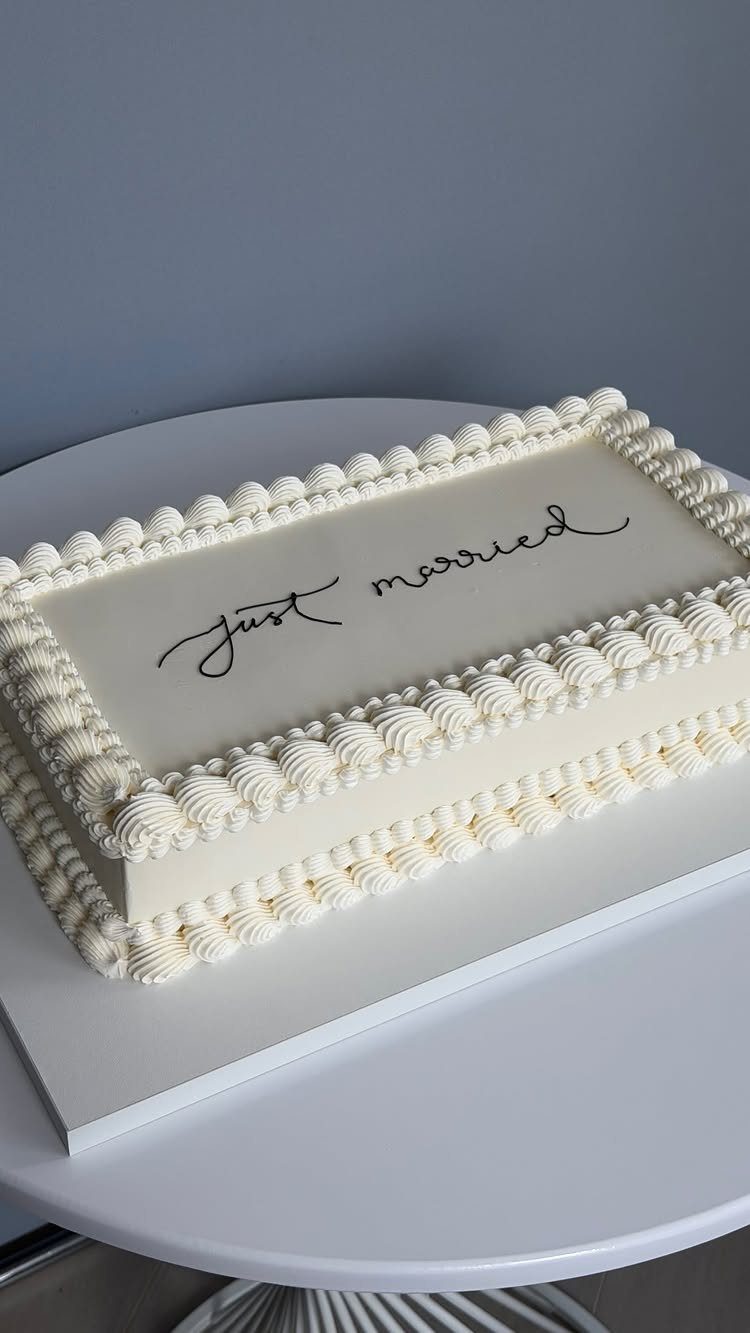 Rectangular white wedding cake with piped frosting and just married written on top