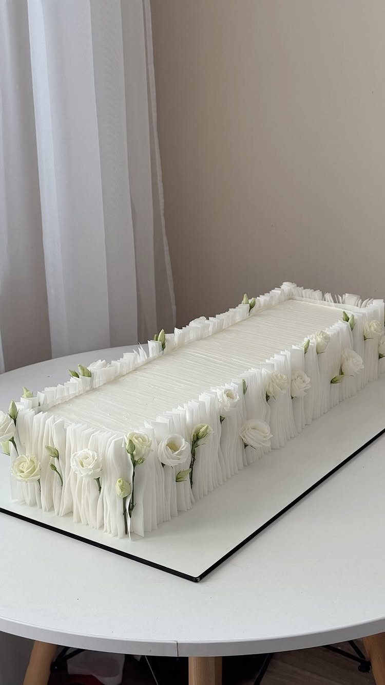 Rectangular white cake with pleated ruffles and small white roses on mirrored base