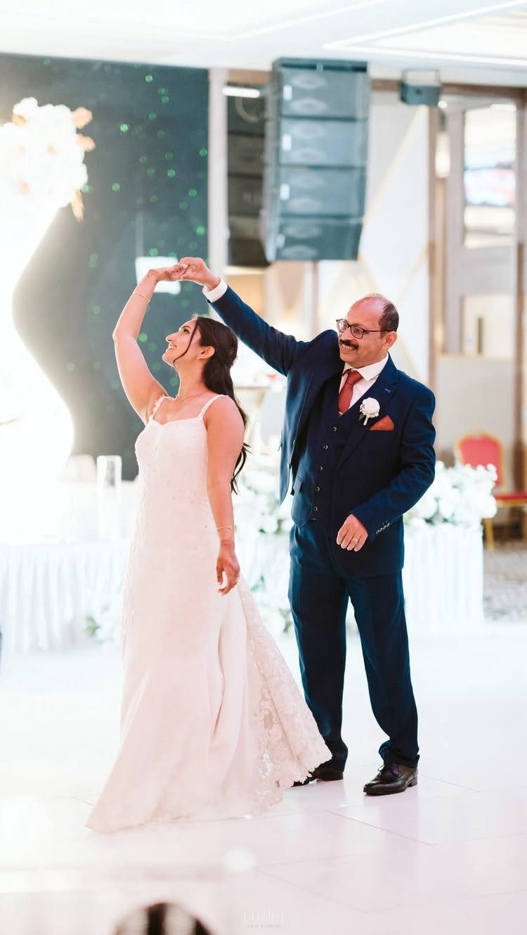 Bride in white gown dancing with her father in a navy blue suit.
