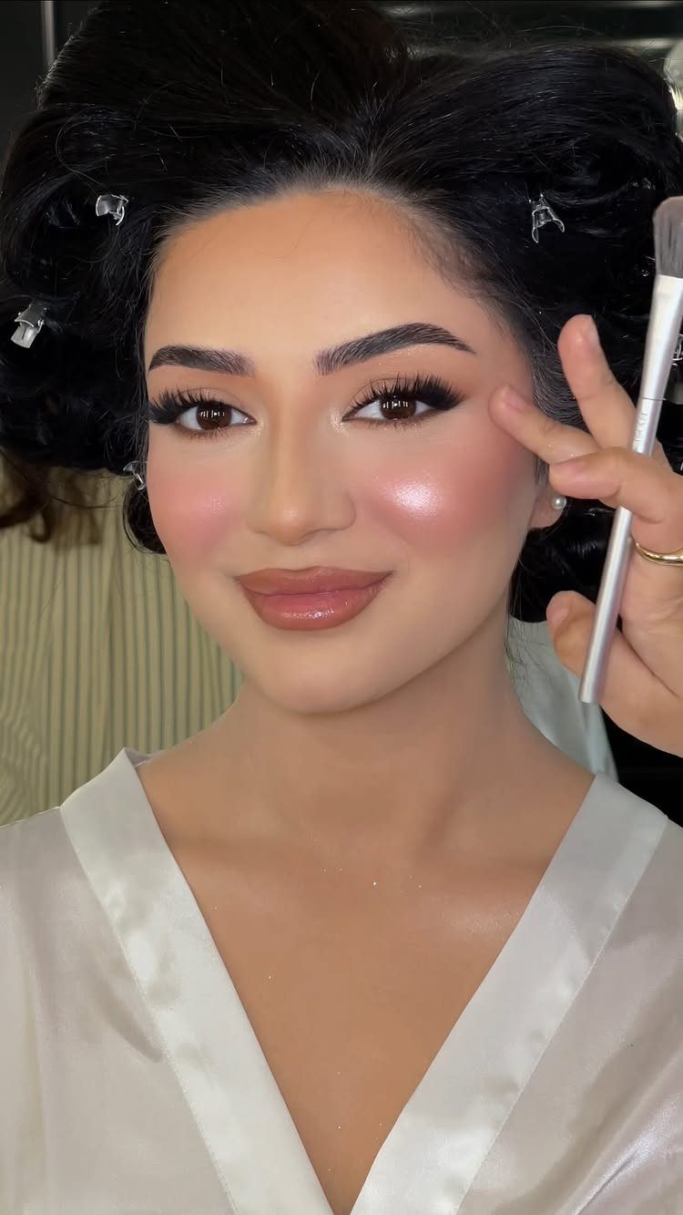 Woman in white robe receiving blush application for a glam bridal makeup look