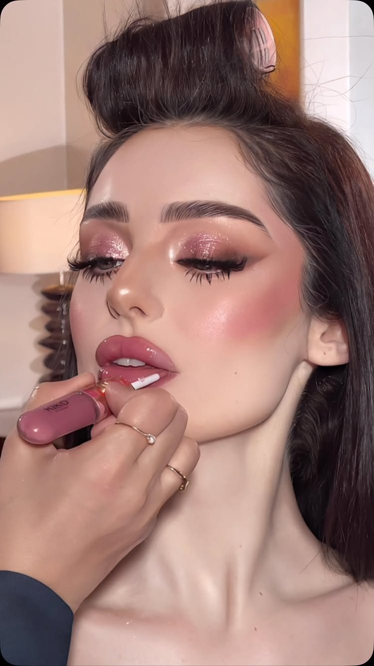 Woman receiving a glossy pink lip application as part of glamorous bridal makeup.