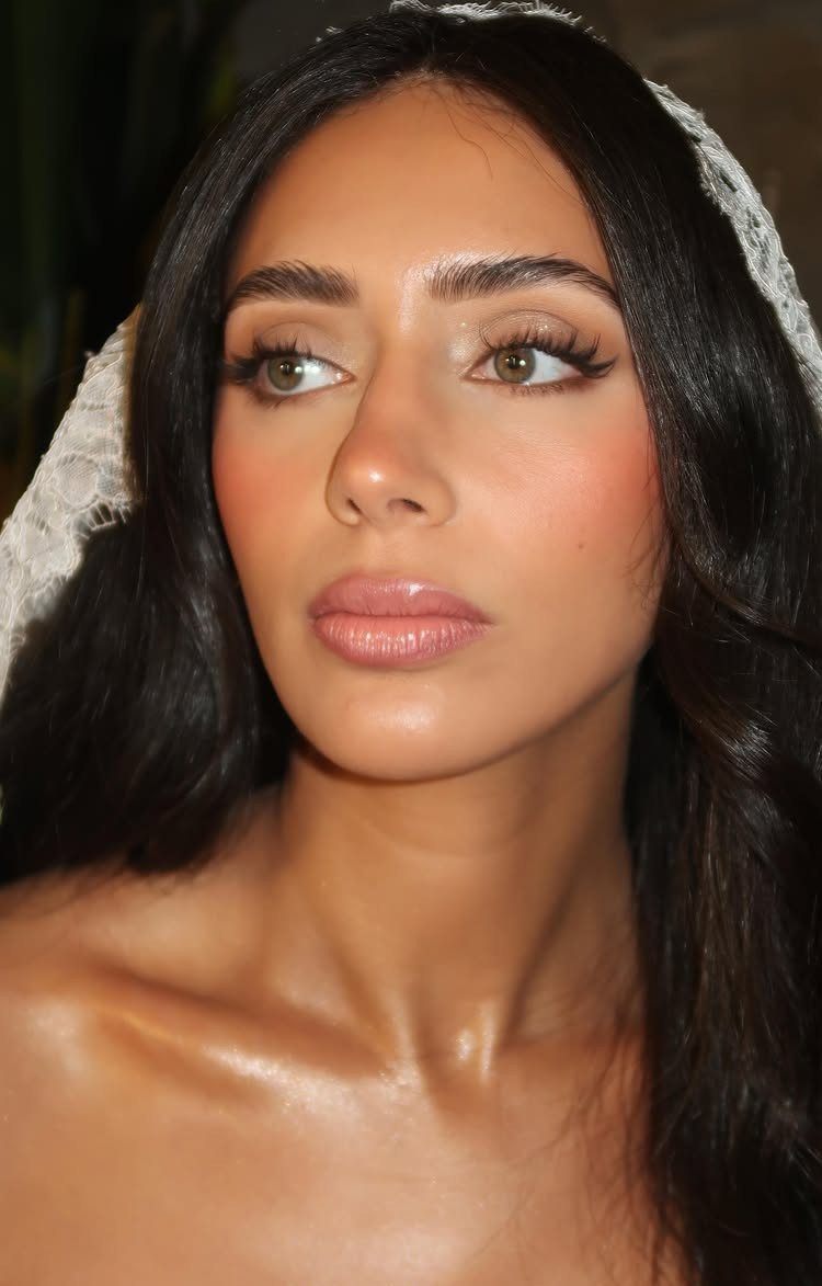 Woman with bridal makeup and a lace veil showing shimmering highlighter on skin