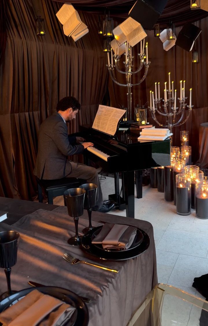 Man in a suit playing a grand piano beside lit candelabras at a dinner.