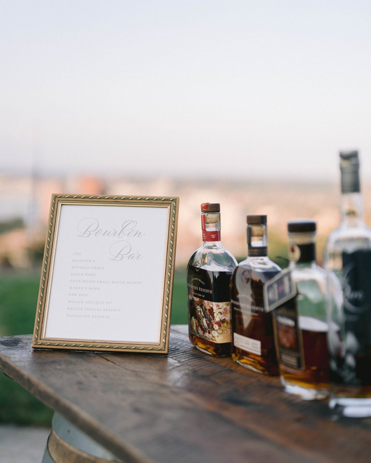 Bourbon bottles and a gold-framed Bourbon Bar sign on a rustic wooden barrel.