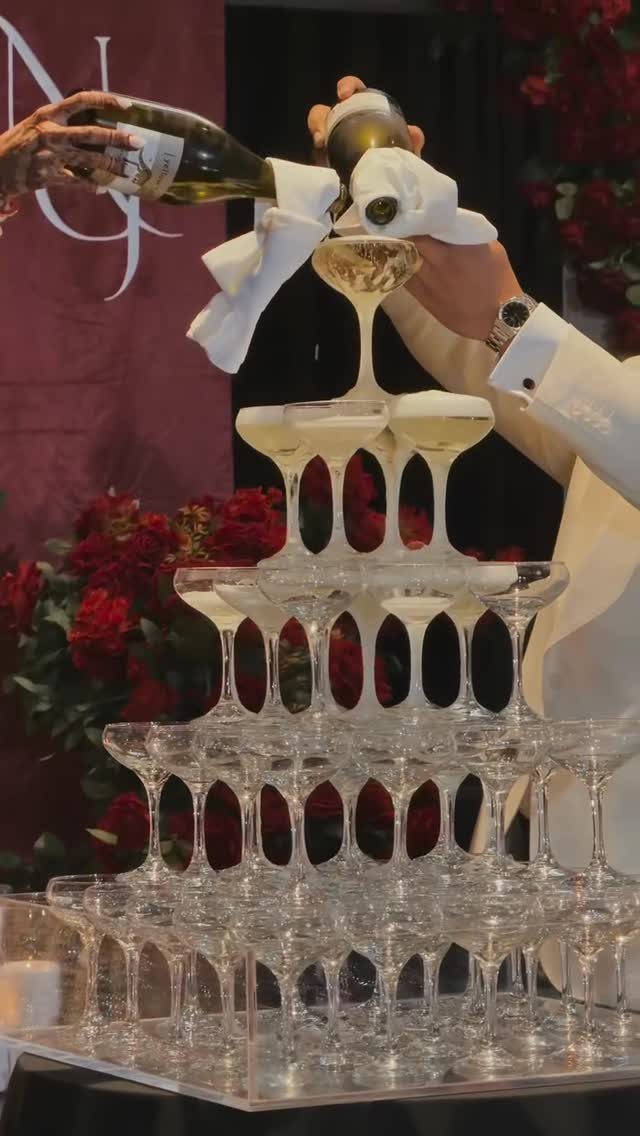 Champagne being poured into a tall tower of stacked coupe glasses at a wedding.