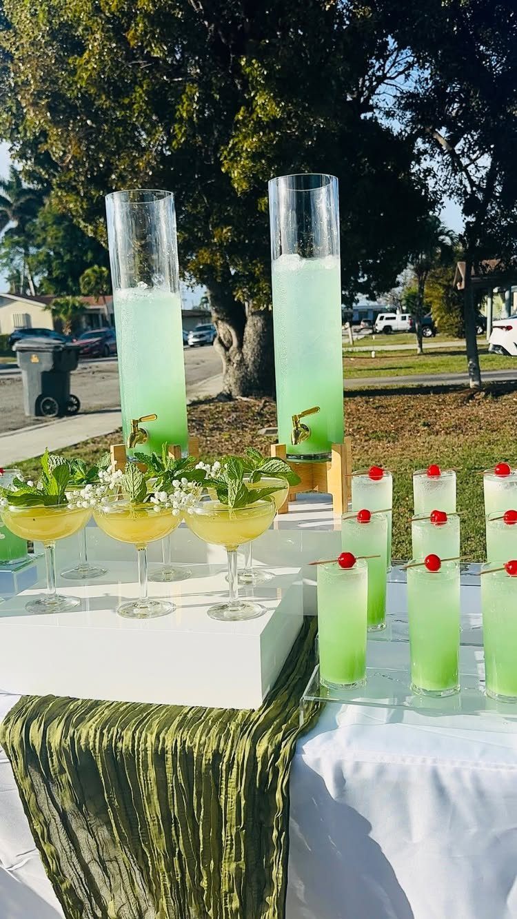 Green and yellow cocktails garnished with fresh mint and white flowers on a table.