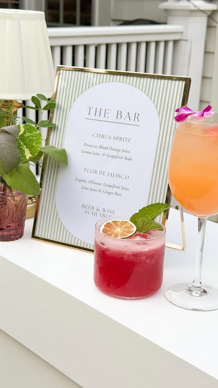 Two colorful cocktails and a framed menu on a white wedding bar counter.