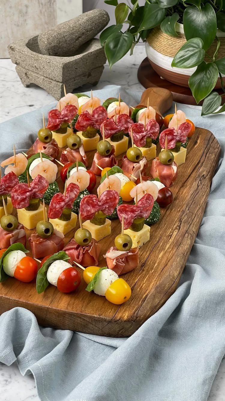 Assorted appetizer skewers with mozzarella, tomatoes, and meats on a wooden serving board.