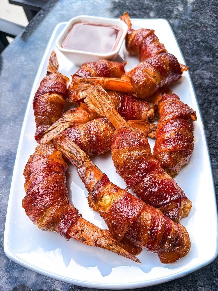 Bacon-wrapped shrimp on a white platter with a side of dipping sauce.
