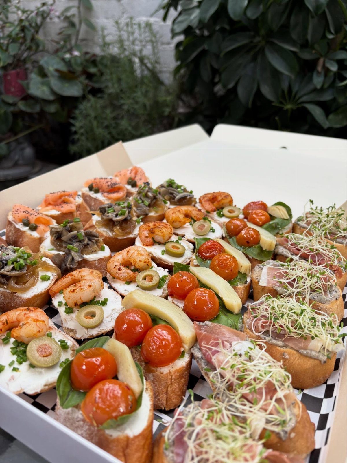 Assorted bruschetta and crostini with shrimp, tomatoes, and meats in a white box.
