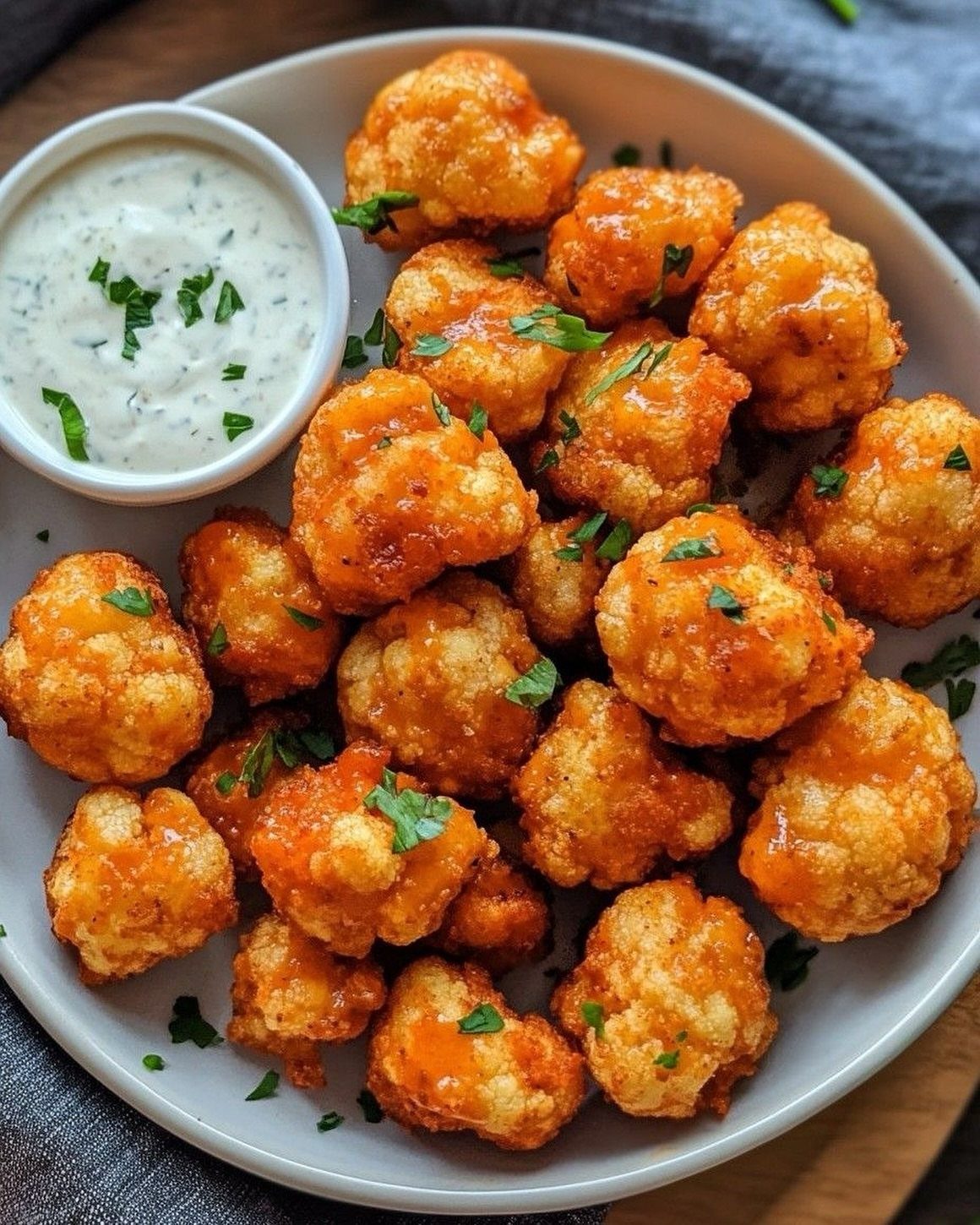 Buffalo cauliflower bites on a white plate with a side of creamy dip.