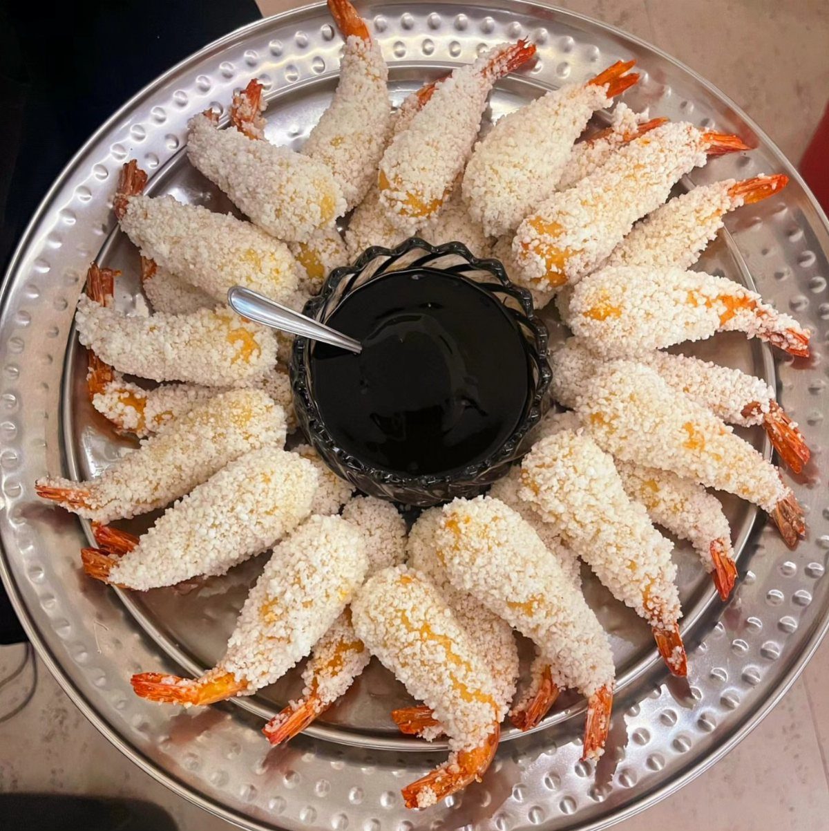 Coconut shrimp arranged in a circle on a silver platter with dipping sauce.