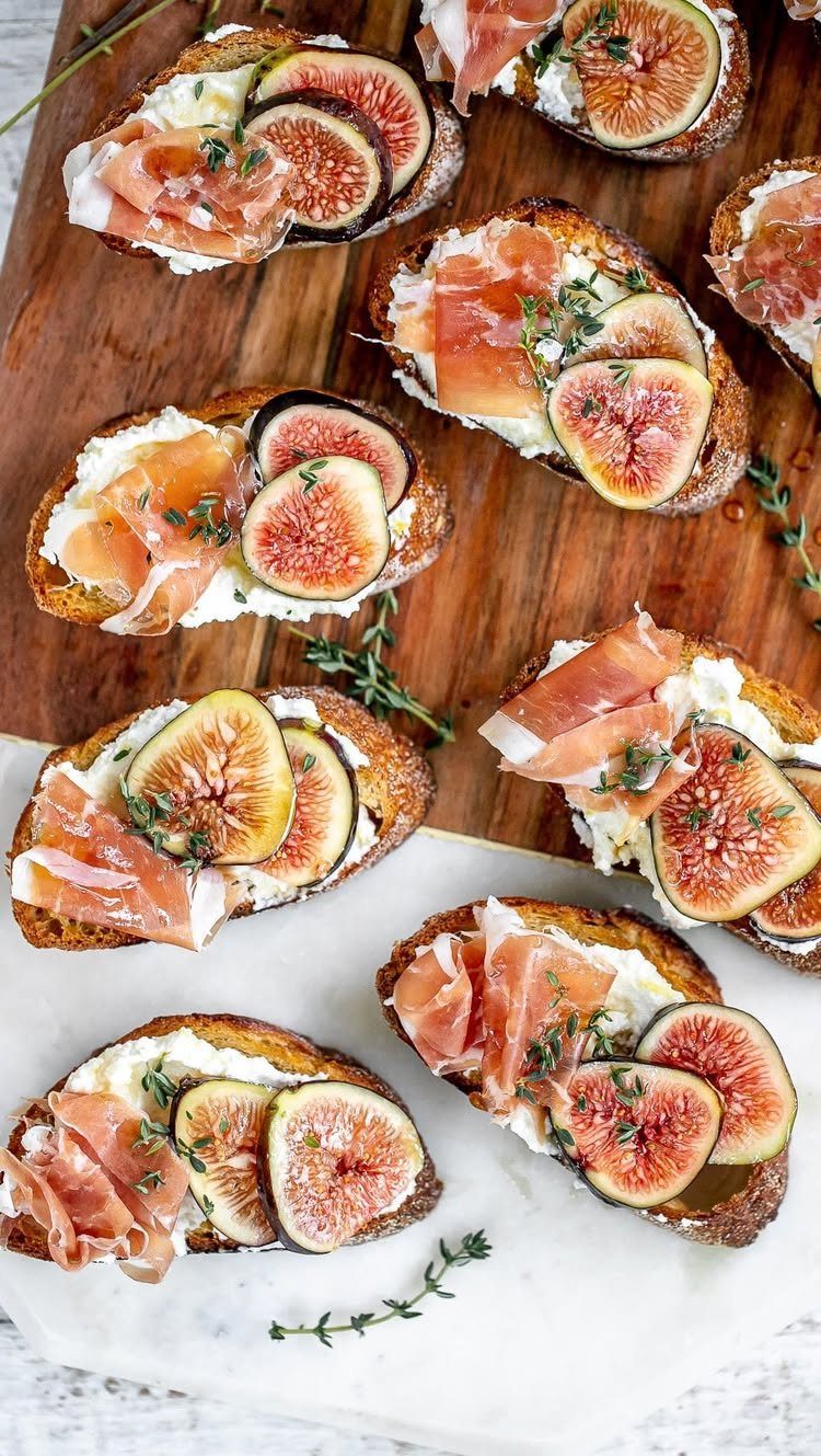 Crostini topped with creamy cheese, prosciutto, and fresh fig slices on a wooden board.