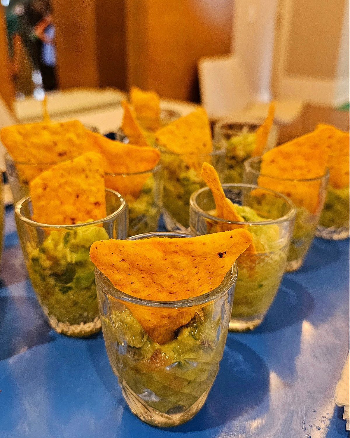 Guacamole in small glass cups with tortilla chips on a blue table