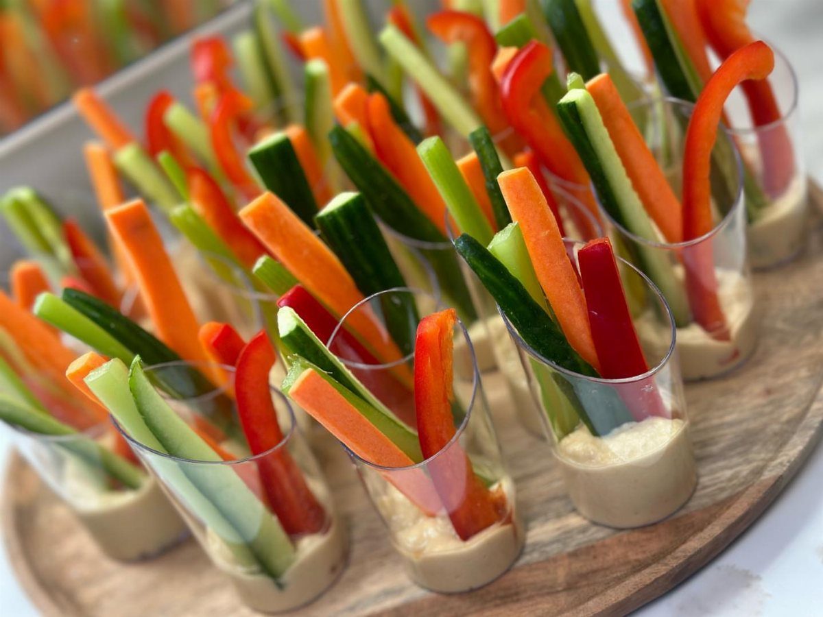 Hummus and veggie cups with carrot, cucumber, and red pepper sticks on a wooden platter