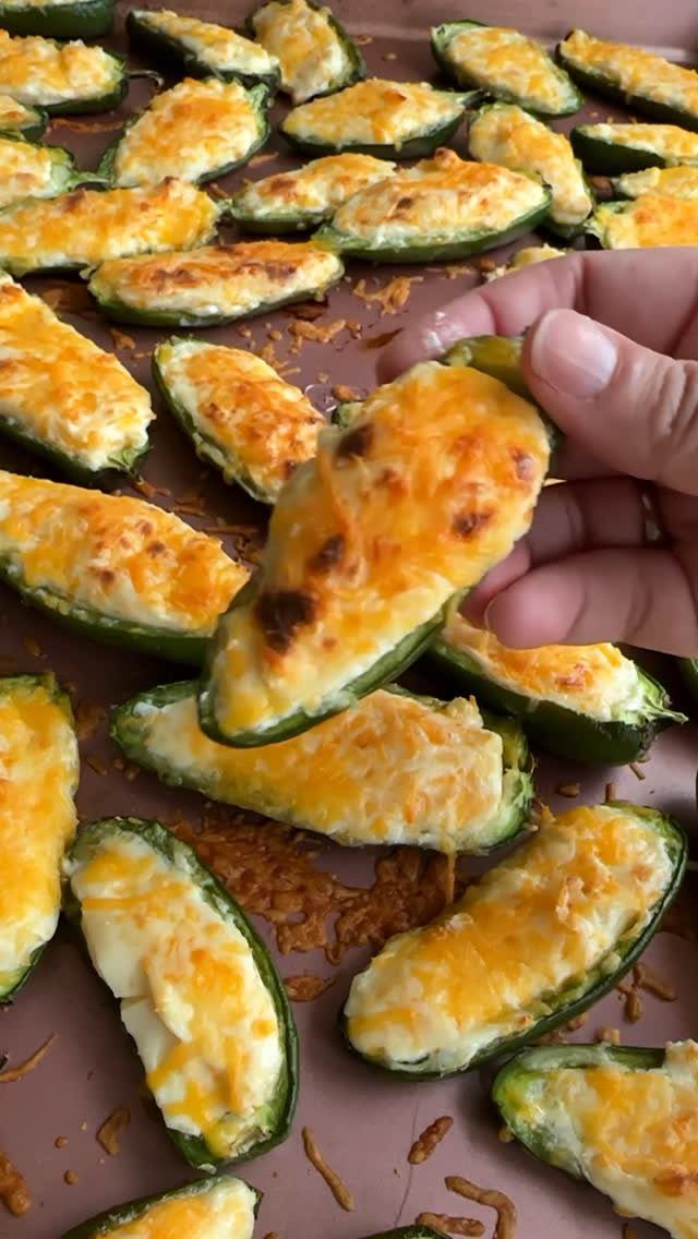 Baked jalapeño poppers filled with melted cheese on a brown baking sheet.