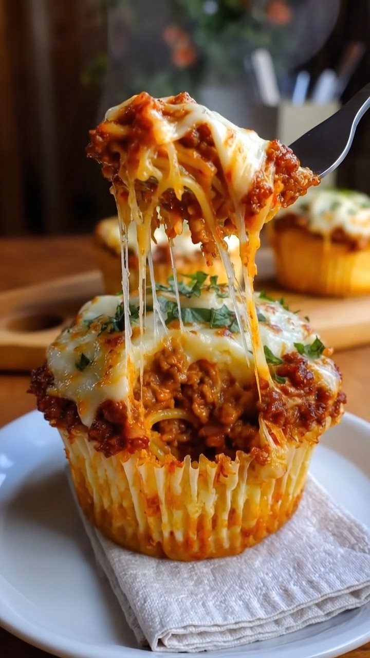 Lasagna cupcake with melted cheese being lifted by a fork on a plate