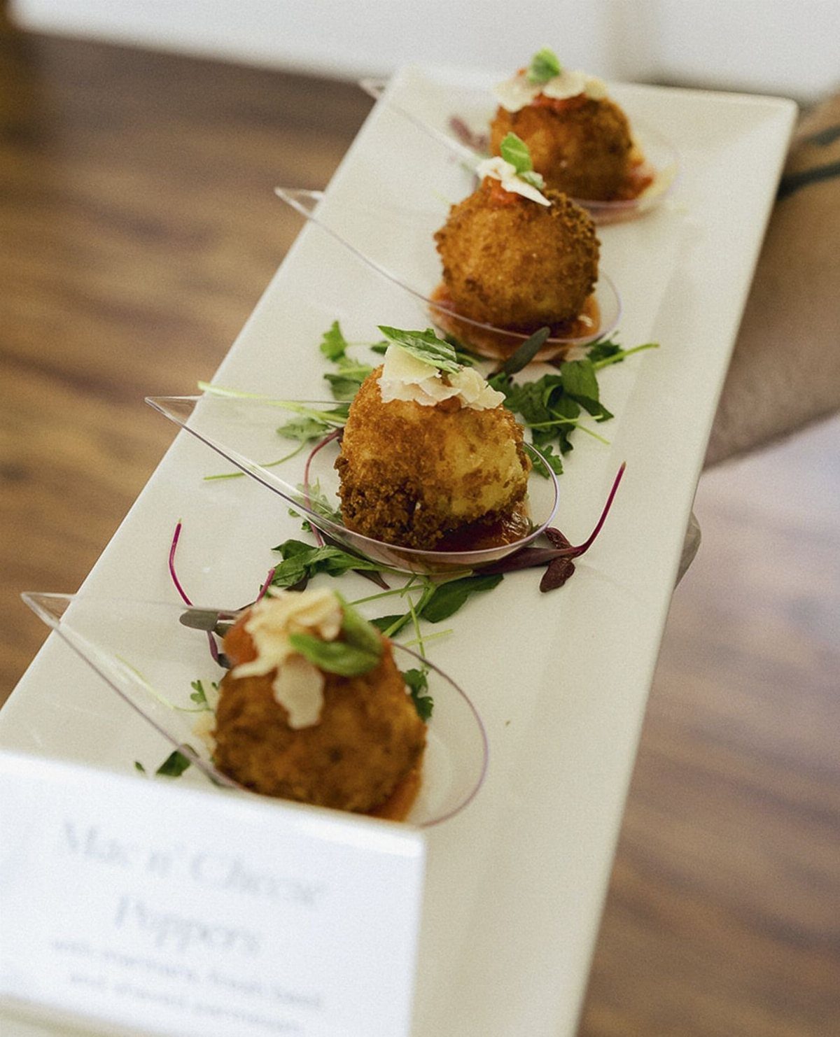 Mac and cheese bites on clear spoons garnished with greens on white platter