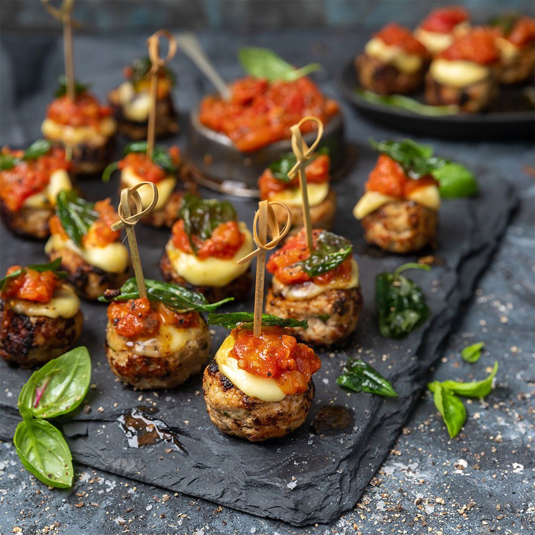Meatballs topped with melted cheese and tomato sauce on a slate platter