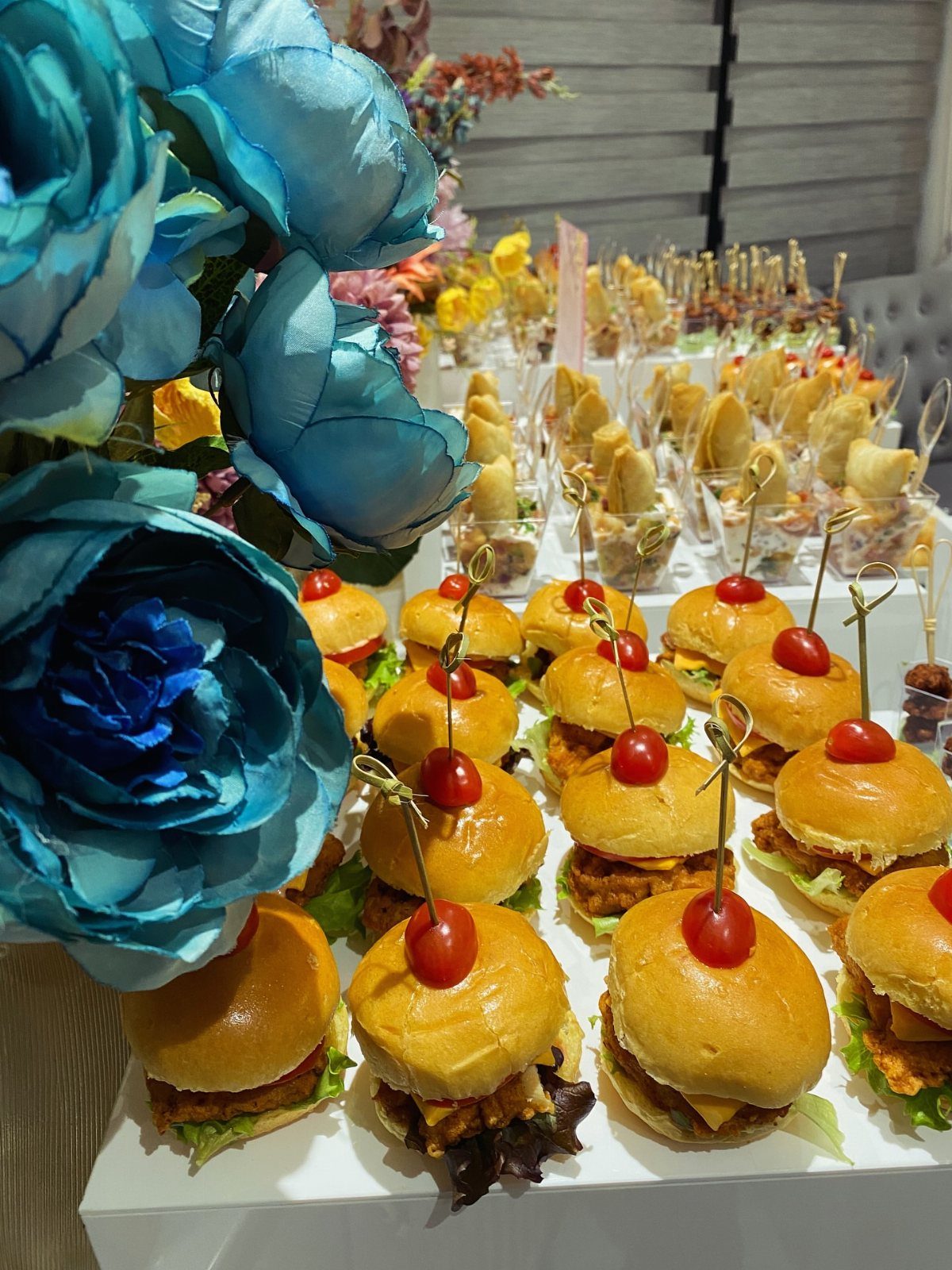 Mini burgers with cherry tomato toppers arranged on a white catering platter.