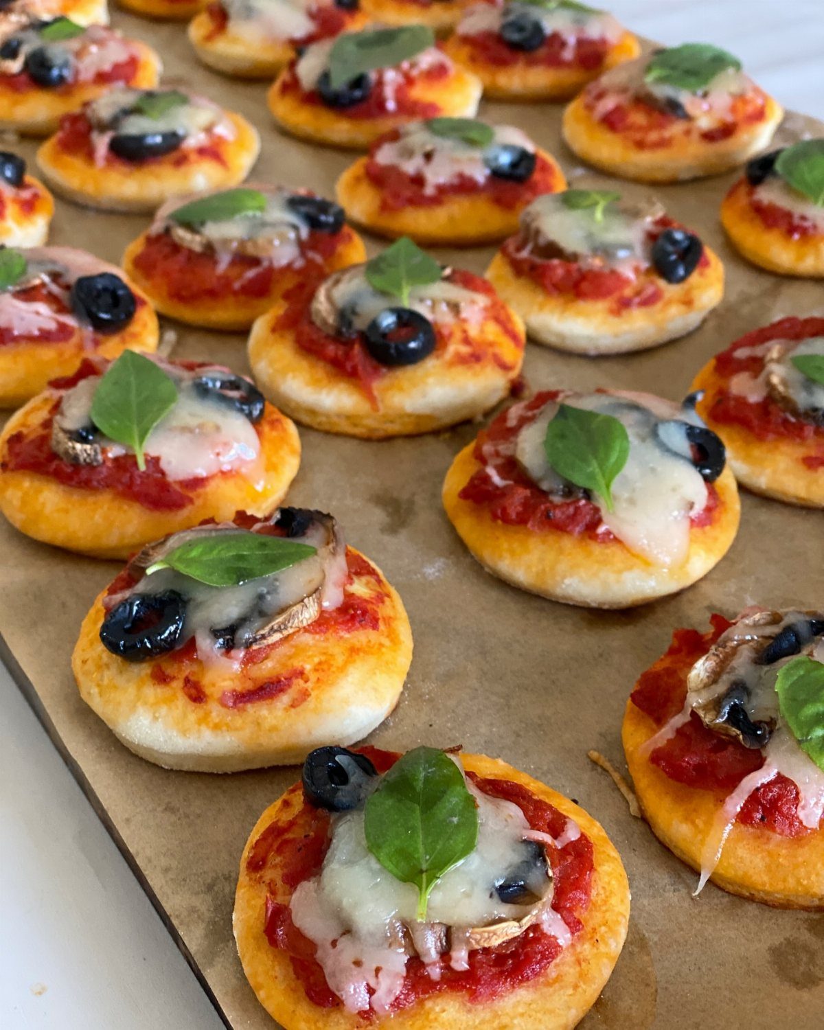Mini pizzas with tomato sauce, melted cheese, olives, and basil on parchment paper.