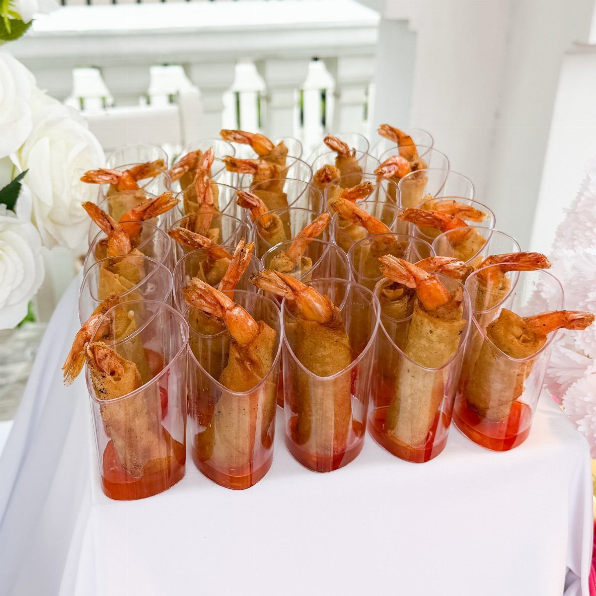 Fried shrimp spring rolls in plastic cups with red sauce on white tablecloth