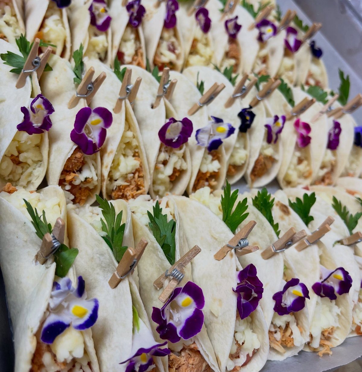 Mini tacos with meat and cheese held by clothespins and purple flowers