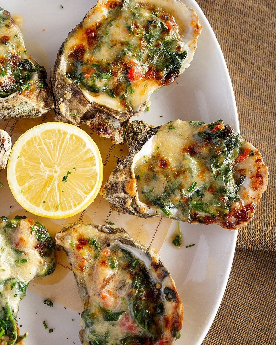 Baked oysters Rockefeller with melted cheese and spinach on a white plate.