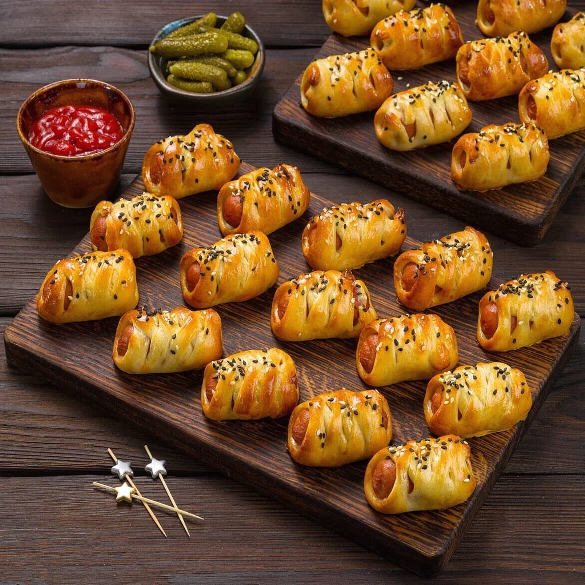 Pigs in a blanket on wooden boards with ketchup and pickles.