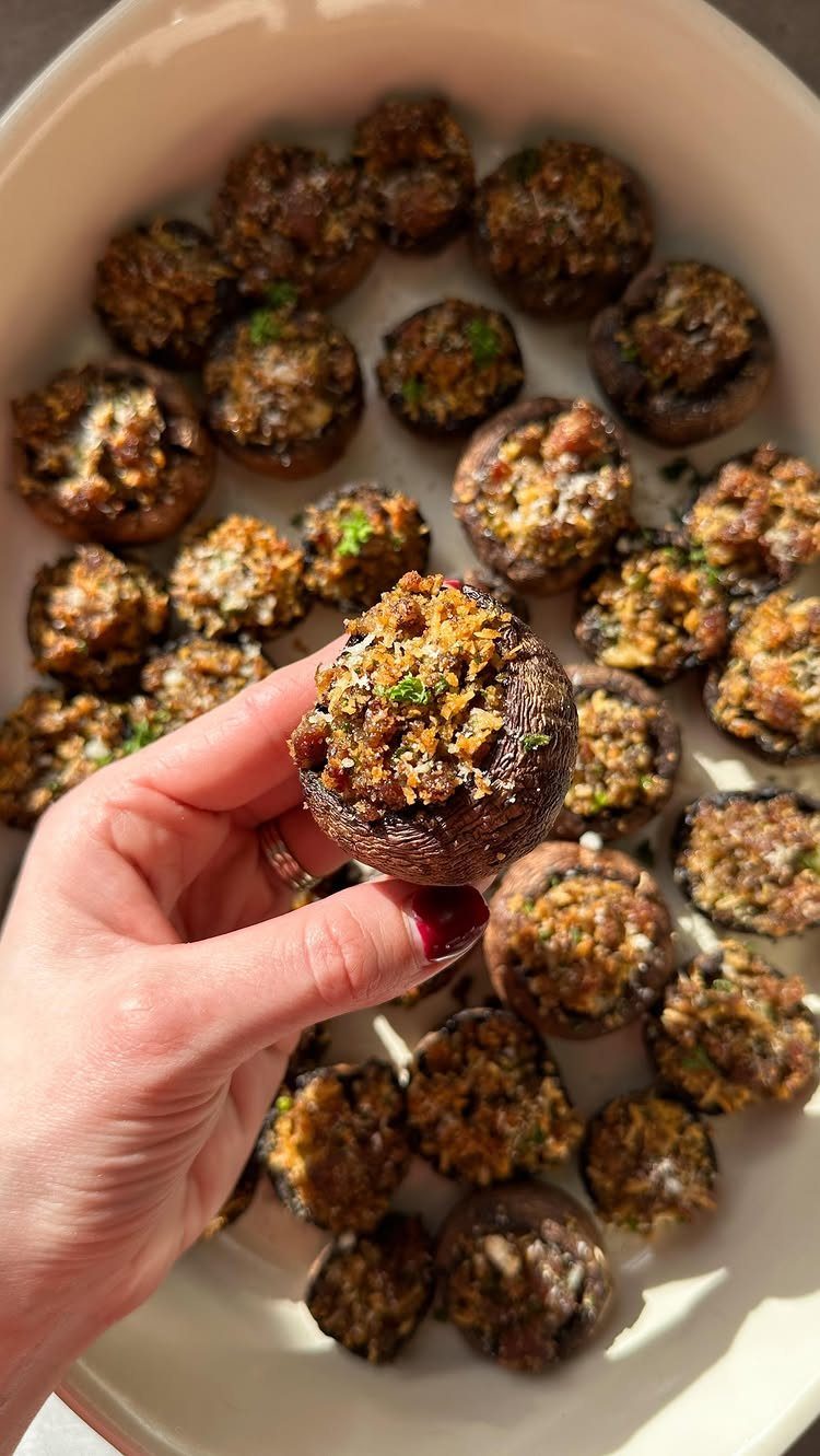 Stuffed mushroom caps on a white platter, one held by a hand.
