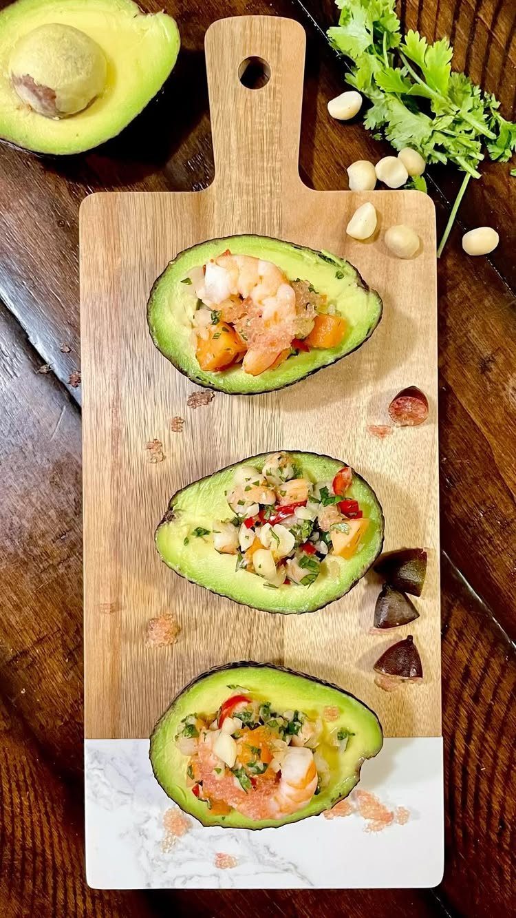 Stuffed avocado halves with shrimp and vegetables on a wooden serving board.