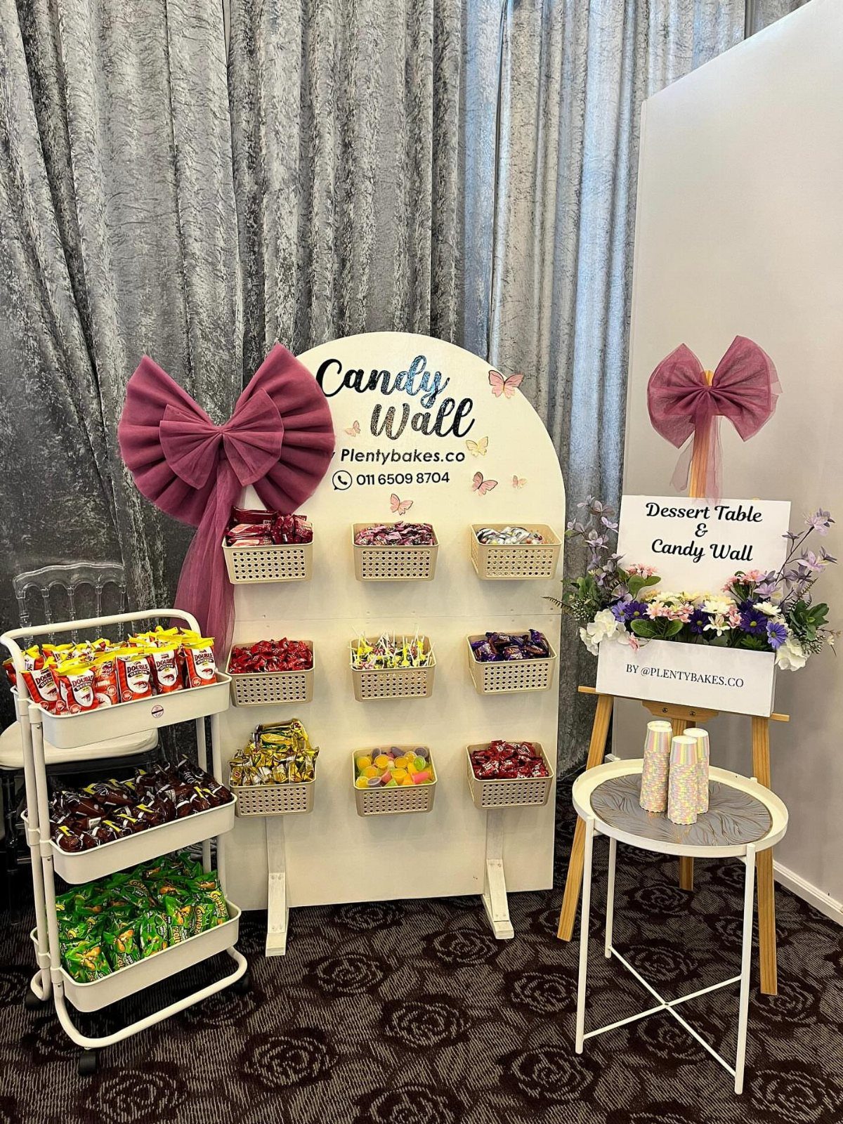 Candy wall with baskets of sweets, purple bows, and a tiered candy cart.