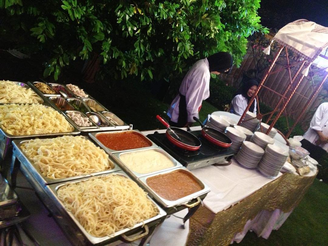 Pasta bar with various noodles and sauces served by a chef outdoors.