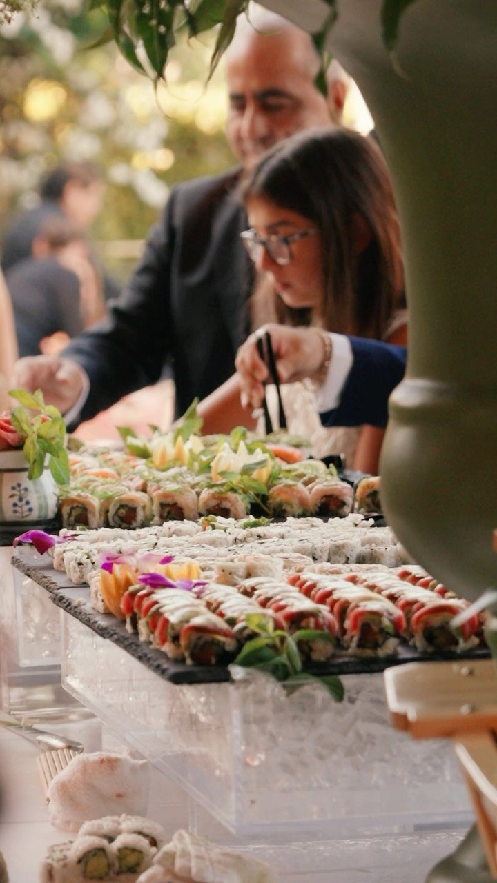 Sushi rolls on black platters at a wedding food station with guests.