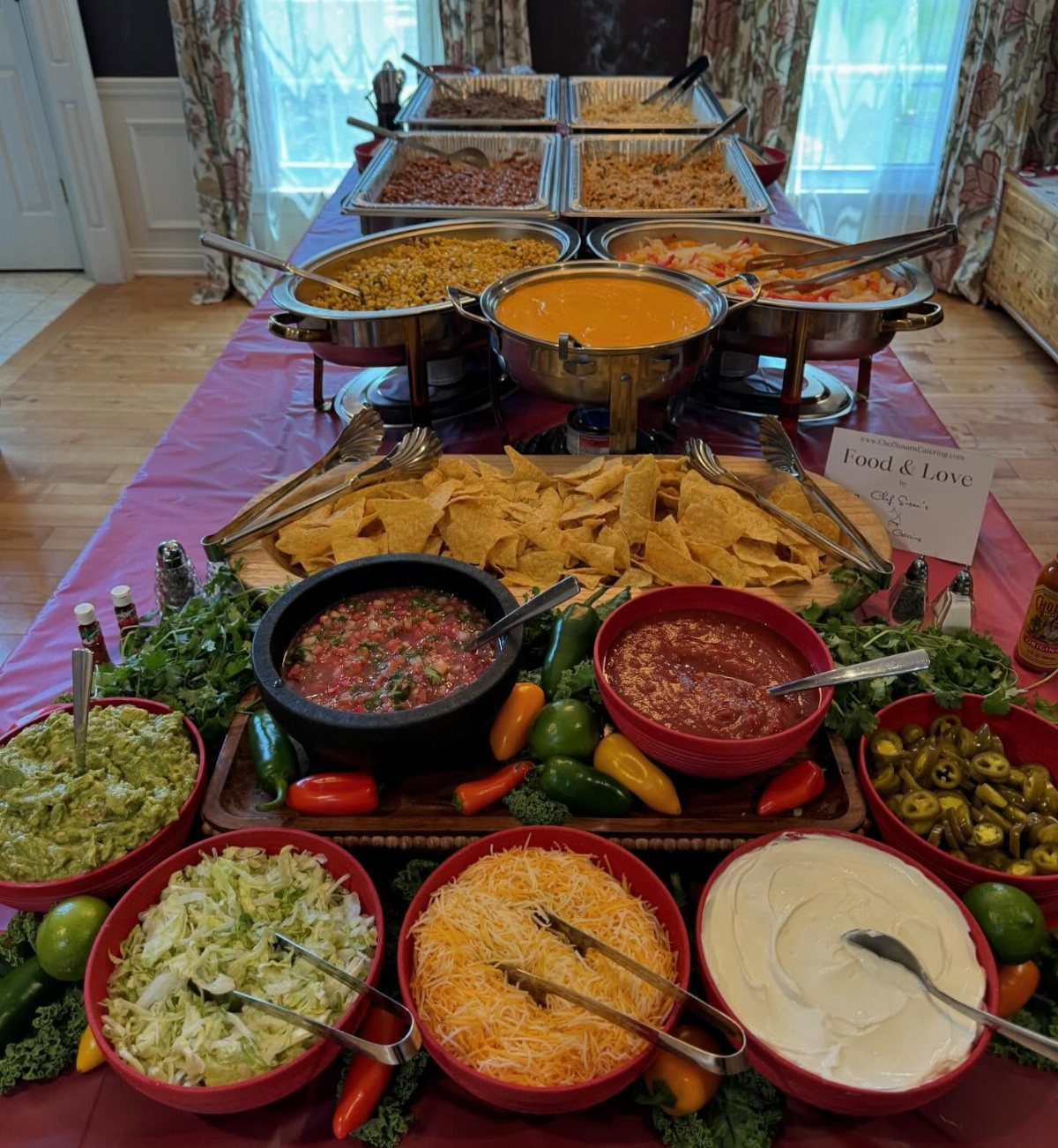 Taco bar buffet with tortilla chips, salsa, cheese, and heated meat trays.