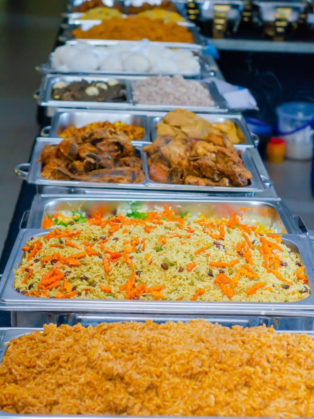 Buffet line of stainless steel trays filled with rice and assorted meats.