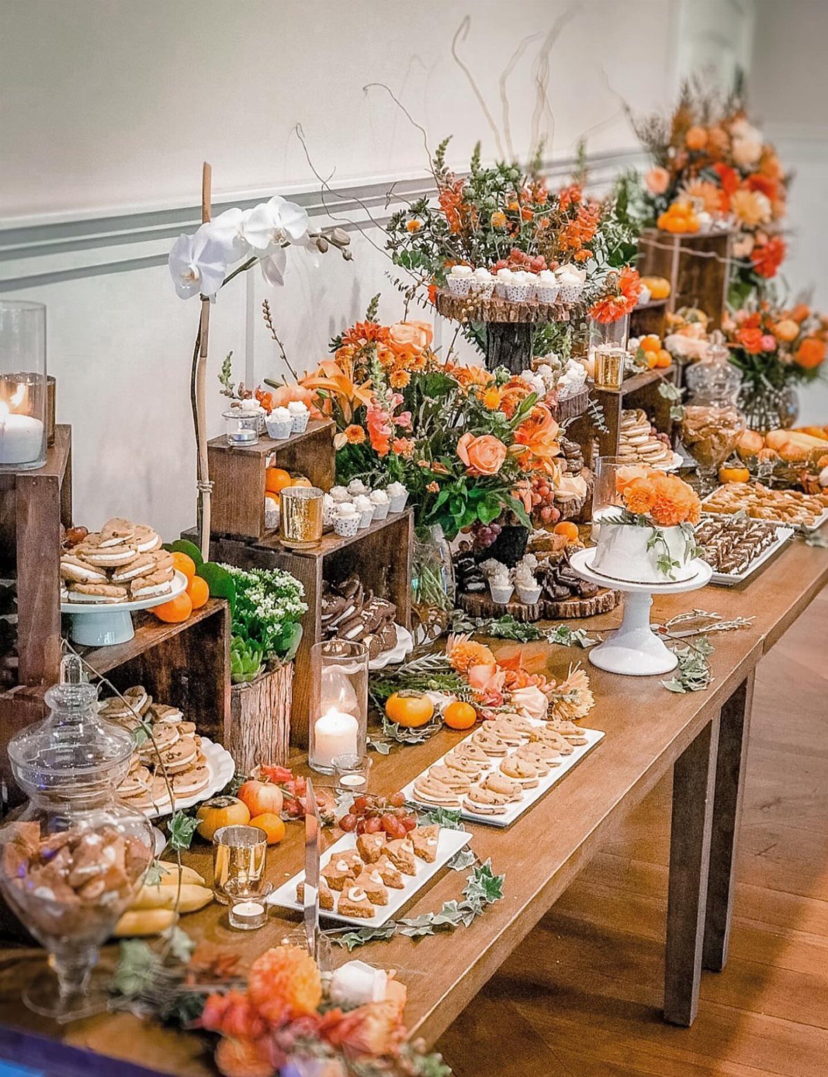 Dessert table with cookies, pastries, and orange flowers at a wedding event.